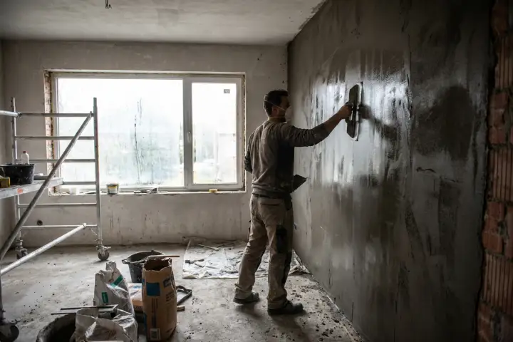 Gipspleister die met een brede stalen spaan op een binnenmuur wordt gepolierd